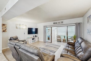 A modern living room with leather sofas, a flat-screen TV, and a sliding glass door leading to a balcony.