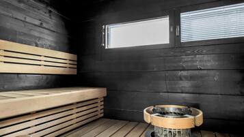 A sauna room with a bench, a fire pit, and a window.