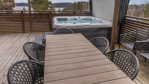 Una terraza de madera con un jacuzzi, sillas de mimbre y una mesa.