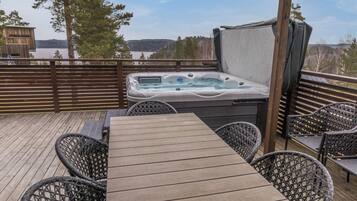 A hot tub on a wooden deck with a view of a lake and trees.
