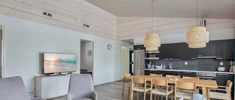 A modern living room with a sofa, chairs, a TV, and a dining area with a table and chairs.