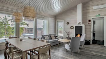 A modern interior with a dining area, sofa, fireplace, and large windows.