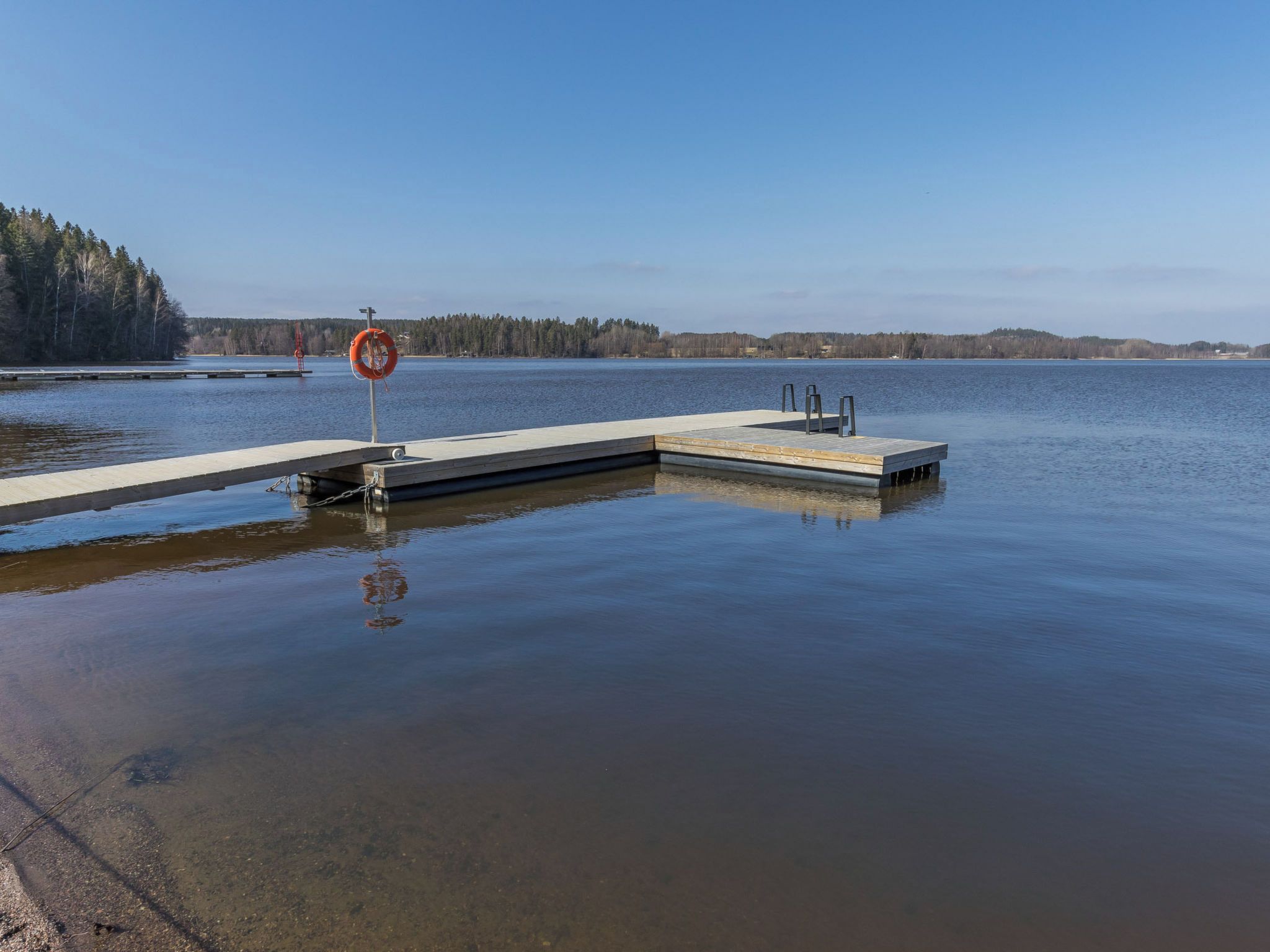 A calm lake with a wooden dock extending into the water, surrounded by trees.