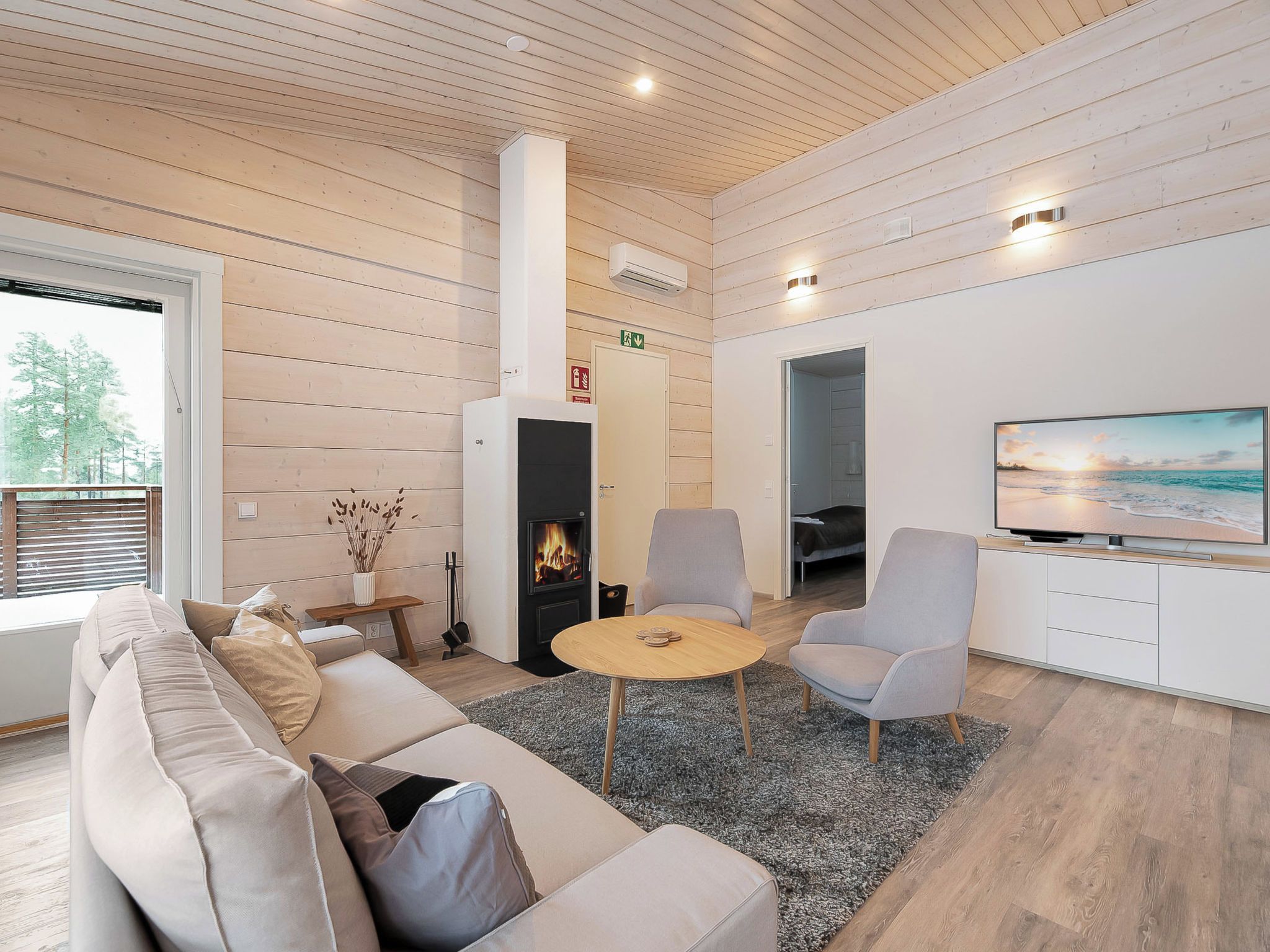 Een moderne woonkamer met een bank, stoelen, een open haard, een televisie en een groot raam.