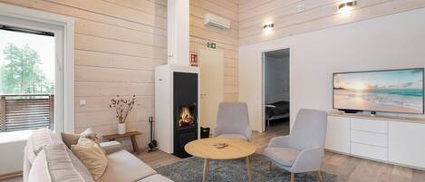 Un salon moderne avec un canapé, des fauteuils, une cheminée, un téléviseur et une grande fenêtre.