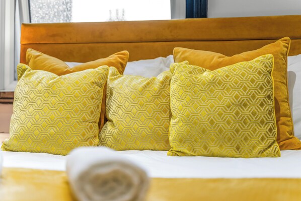 Una cama con cabecera de madera y varios almohadones con diseños geométricos.