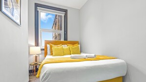 Una habitación de hotel con una cama, una ventana, una lámpara y un cuadro en la pared.