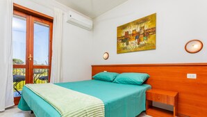 Ein Schlafzimmer mit einem Bett, einem Nachttisch, einem Gemälde und einem Fenster mit Vorhängen.