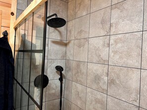 Una ducha con puerta de vidrio, paredes de azulejos y techo de madera.