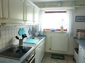 Une cuisine avec des meubles blancs, une cuisinière, un évier et une fenêtre donnant sur l’extérieur.