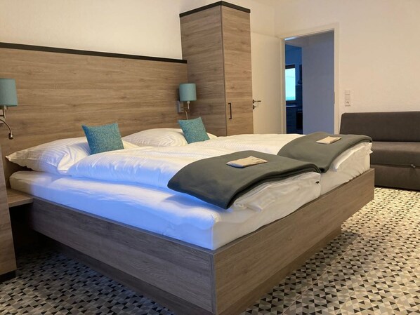 Une chambre à coucher avec un lit en bois, deux oreillers, une table de chevet, une armoire et une porte donnant sur une autre pièce.