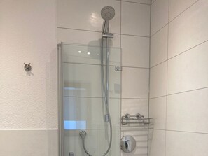 Une douche fermée par des parois en verre, dotée d’un pommeau de douche à main, d’un robinet mural et d’un porte-serviettes.