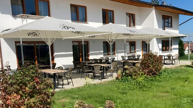 Een gebouw met terras en parasols, omgeven door groen.