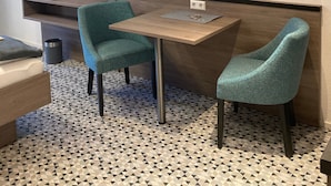 Een moderne kamer met een aan de muur bevestigde televisie, een klein tafeltje met stoelen en een vloer met een geometrisch patroon.