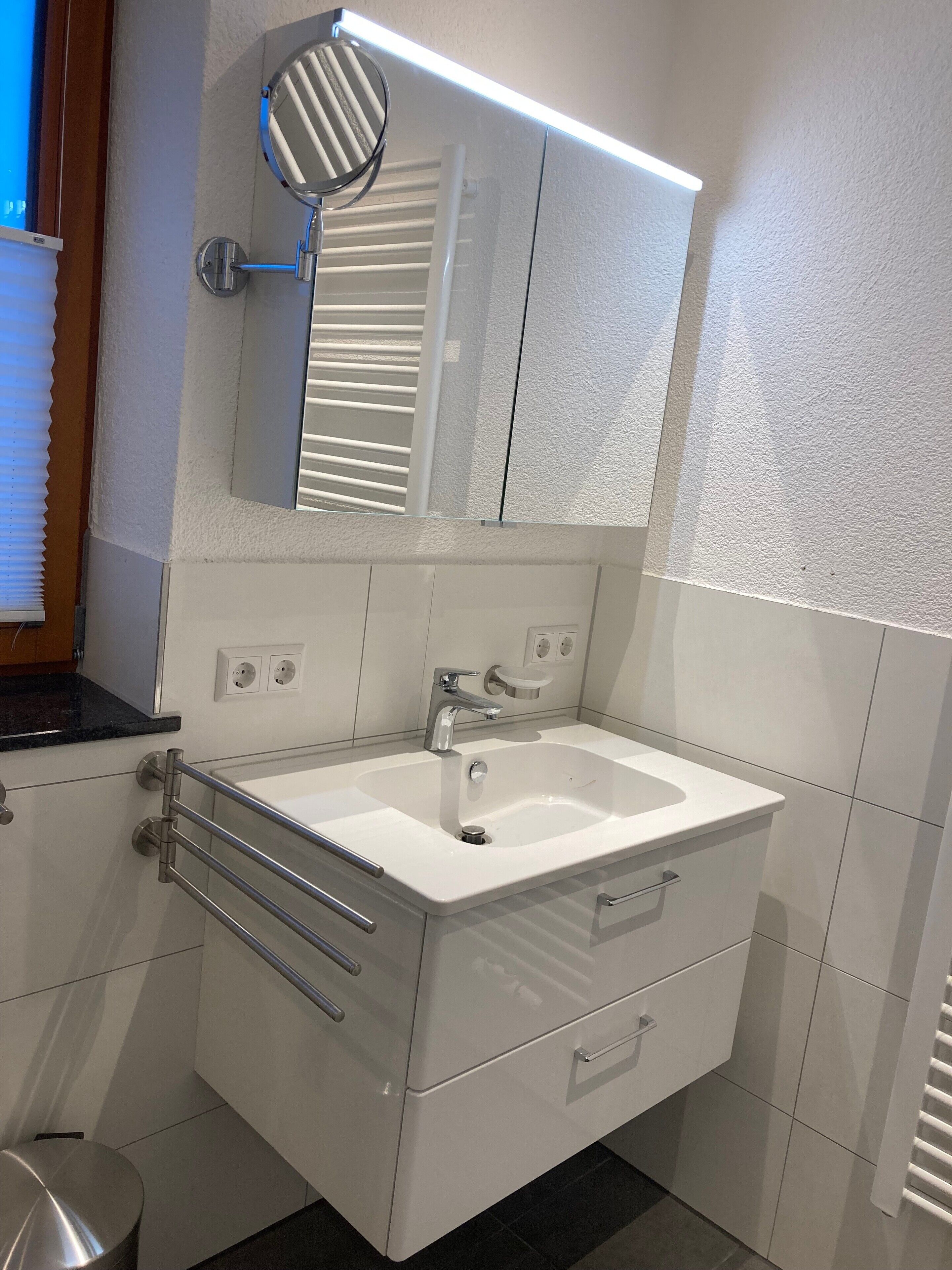 Un baño con lavamanos blanco, espejo y toallero.