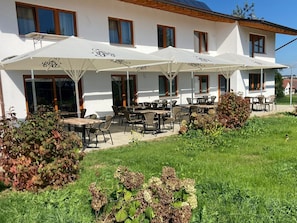 Ein Gebäude mit Außenplätzen, weißen Sonnenschirmen und einem Garten.