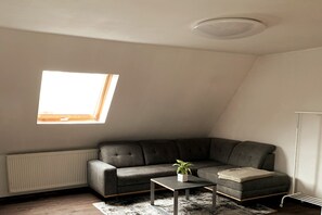 A room with a sectional sofa, a small table with a plant, a radiator, and a skylight.
