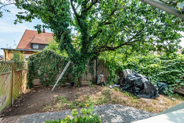 Un patio trasero con un árbol, una cerca de madera y un camino de ladrillo.