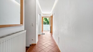 A narrow hallway with white walls, a radiator, and a tiled floor.