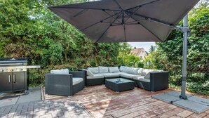 An outdoor patio with a sectional sofa, a grill, and a large umbrella.