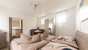 A bedroom with a bed, bedside tables, a mirror, and a view of the kitchen.