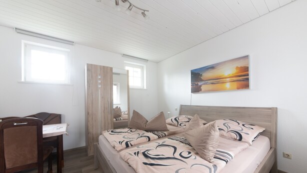 A bedroom with a bed, a desk, a chair, and a window.