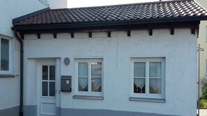 A small, single-story building with a white facade, a tiled roof, and a small porch area.