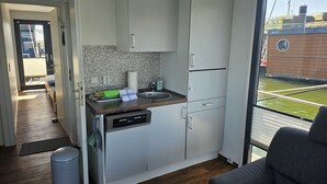 Cozinha compacta com armários brancos, lava-louças e janela com vista para um edifício e áreas verdes.