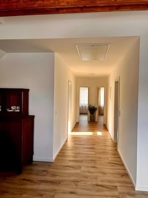 Un pasillo con suelo de madera, paredes blancas y un armario de madera a la izquierda.