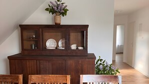 Een eethoek met een houten tafel, stoelen, een fruitmand en een kast met glazen deuren.