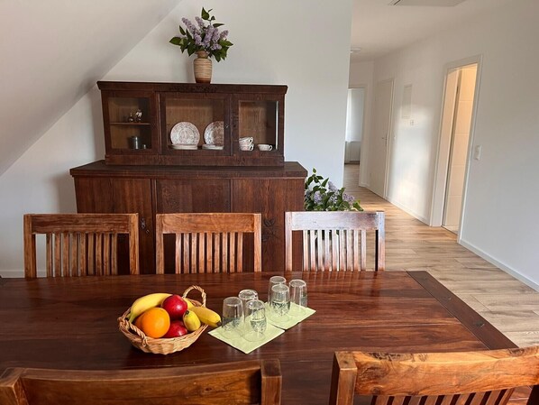 Un comedor con una mesa de madera, sillas, una cesta de frutas, saleros y pimenteros, y un aparador con puertas de vidrio.