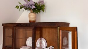 Een houten kast met glazen deuren, gevuld met gestapelde borden, bekers en een vaas met bloemen.
