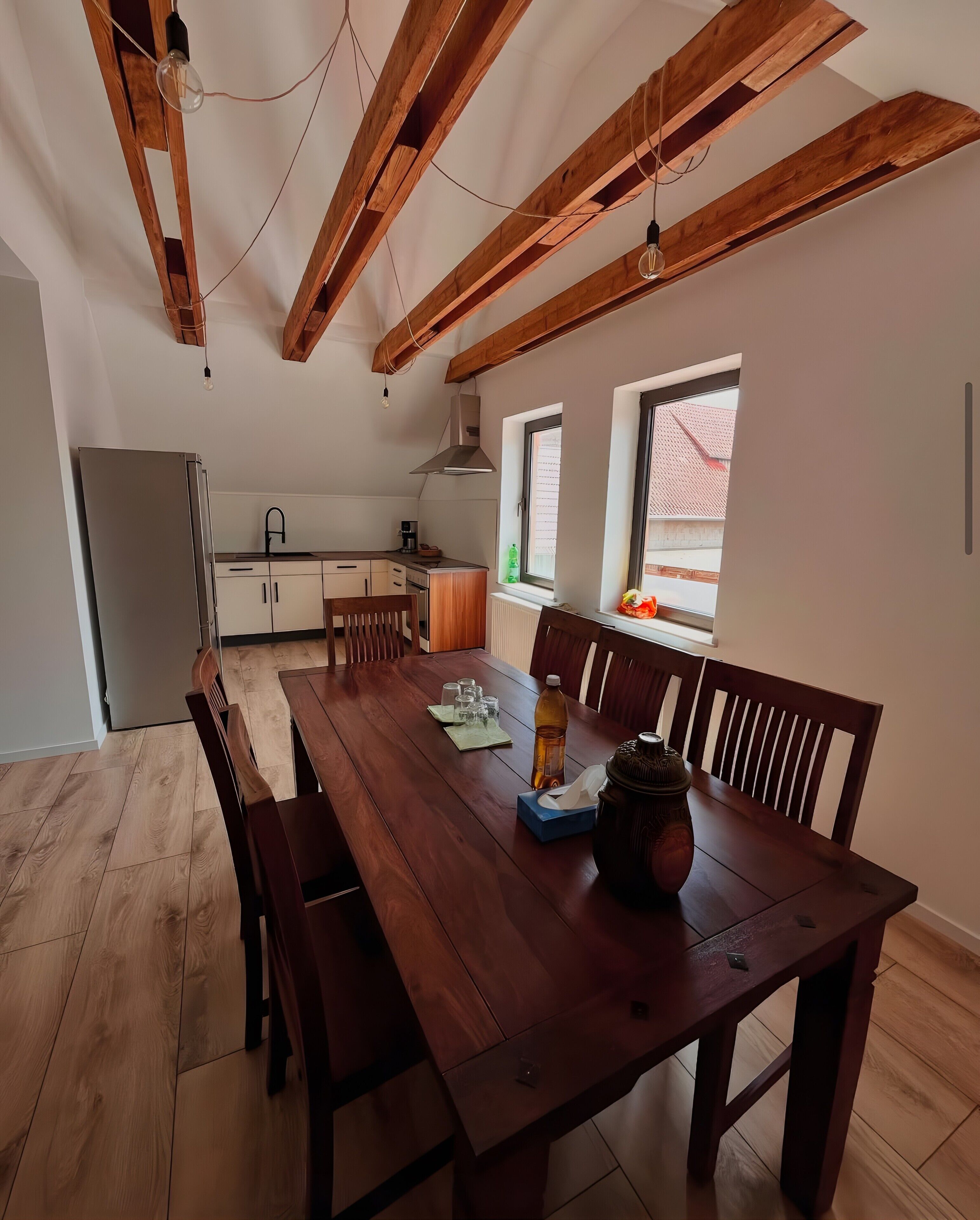 Een moderne keuken met houten balken, een eettafel met stoelen en een koelkast.