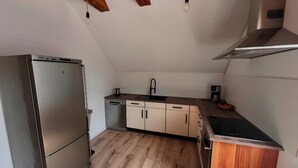 Een kleine keuken met een koelkast van roestvrij staal, houten kastjes, een houten aanrecht, een spoelbak en een fornuis.