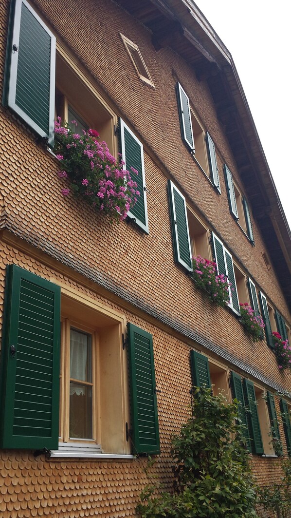 A multi-story building with green shutters, brick walls, and flower boxes on the windowsills.