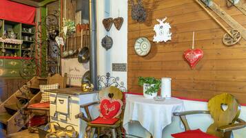 Een rustiek interieur met houten wanden, een oude fornuis en diverse decoratieve items, waaronder hartvormige versieringen en een houten stoel.
