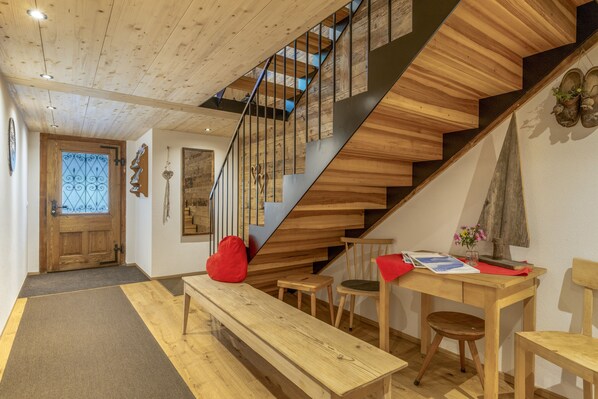 A wooden staircase with a modern design, a bench, a table with a vase of flowers, and a wooden door.