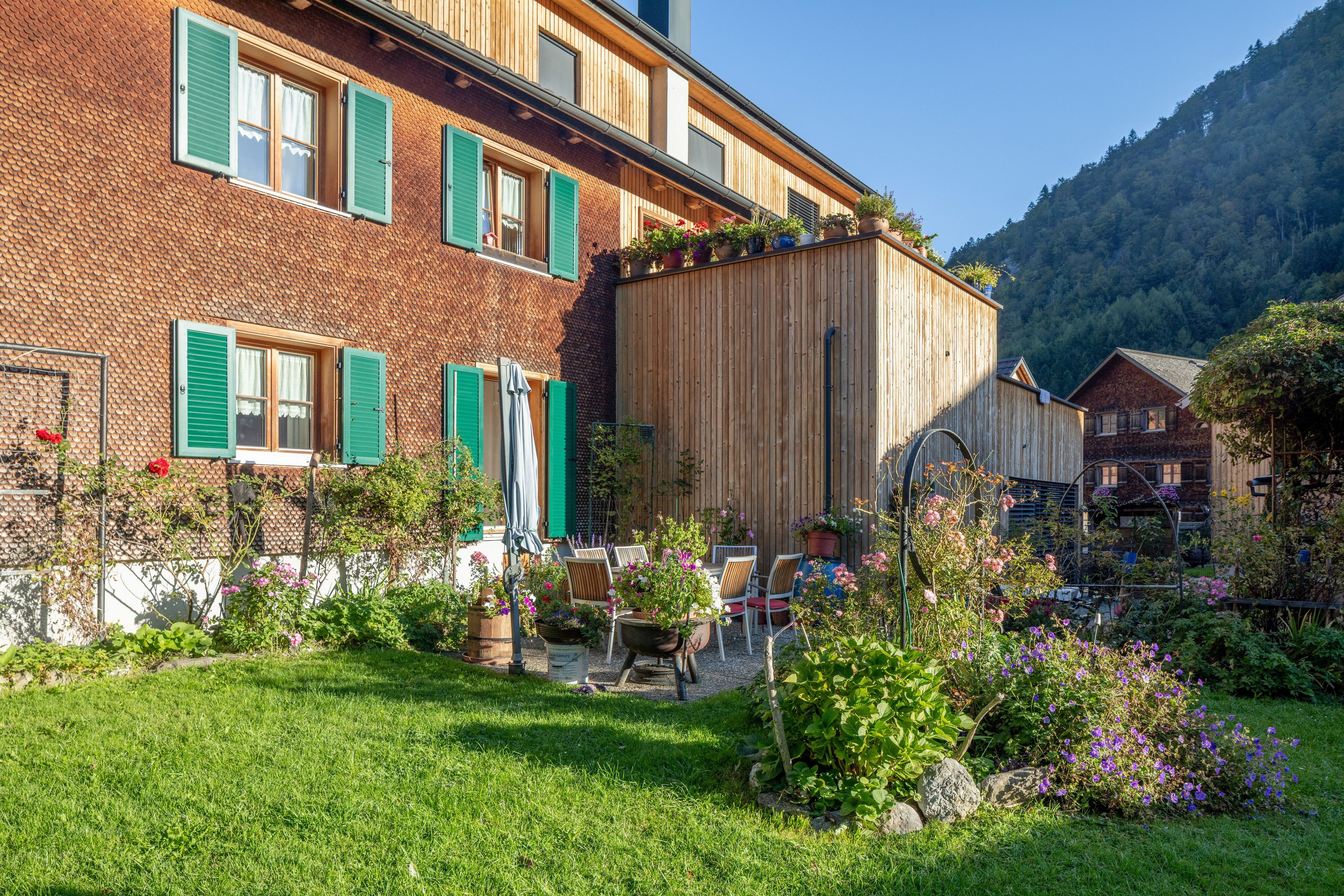 Ein traditionelles Chalet mit Backsteinfassade, grünen Fensterläden und einem Holzanbau.