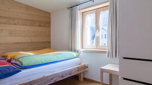 Un dormitorio con una cama de madera, una mesita pequeña y una ventana con cortinas.
