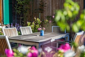 A wooden table with chairs, a blue vase with flowers, and a wooden fence in the background.