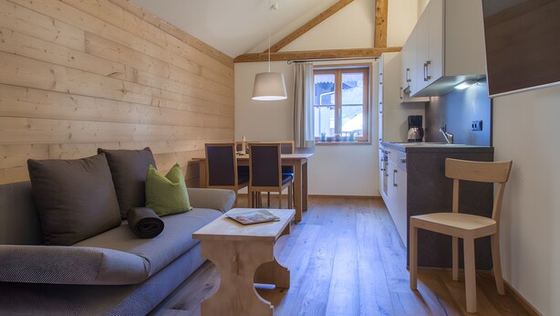 Interior acogedor de una cabaña, con paredes de madera, un sofá, una mesa de comedor y una zona de cocina.