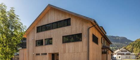 A modern wooden building with a sloped roof, large windows, and a visible entrance.