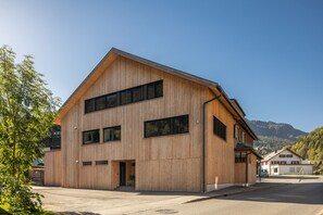 A modern wooden building with a sloped roof, large windows, and a visible entrance.
