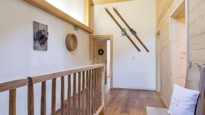 Una escalera de madera con barandilla, una puerta de madera adornada con un adorno, y un par de esquíes colgados en la pared.