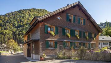 Ein traditionelles Chalet mit geneigtem Dach, zahlreichen Fenstern mit Fensterlädchen und einem Balkon mit Topfpflanzen.