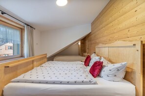 Une chambre avec un plafond en pente en bois, une fenêtre avec des rideaux et un lit avec une literie et des oreillers à motifs.