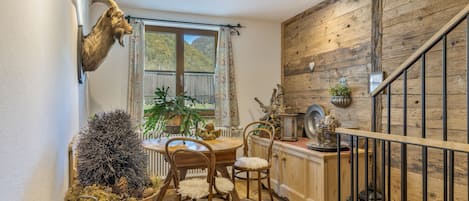 A rustic interior with a wooden staircase, a dining area with wooden chairs, and a mounted animal head.
