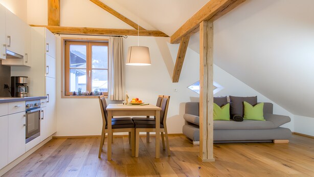 A modern kitchen with wooden beams, a dining table, and a gray sofa with green cushions.