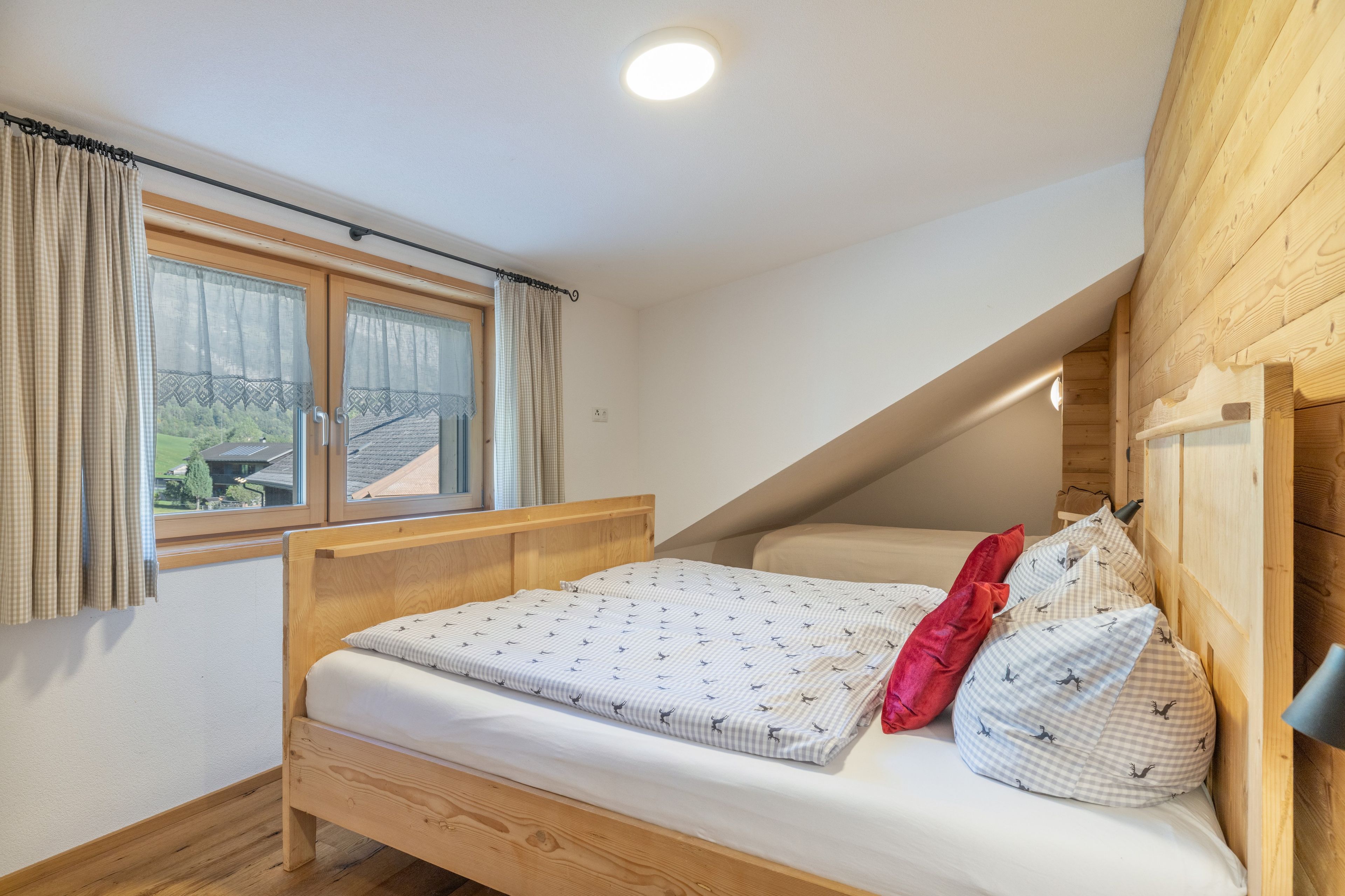 Ein Einzelbett mit Kopfteil, ein Fenster mit Vorhängen und eine geneigte Decke.