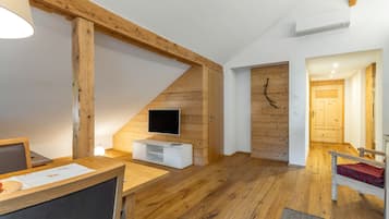 Ein modernes Wohnzimmer mit Holzbalken, einem Flachbildfernseher, einer weißen Unterhaltungsanlage und einer gemütlichen Sitzecke mit einem roten Kissen.